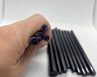 May include: A collection of dark purple, cylindrical, hollow plastic tubes. Several tubes are held together in a cluster, showing their circular openings, while the remaining tubes are arranged in a parallel row on a white surface.