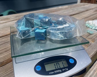 May include: A clear plastic bag filled with small, square, blue and light blue striped tiles resting on a digital kitchen scale. The scale display shows a weight of 101 grams, with a maximum capacity of 5000 grams and a graduation of 1 gram.