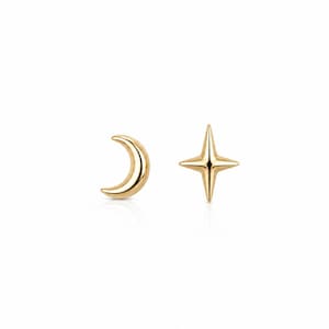 May include: A pair of gold-toned stud earrings featuring a smooth, polished finish. One earring is shaped like a crescent moon, while the other is shaped like a four-pointed star with elongated, tapered tips. Both pieces have a reflective surface.