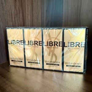 May include: Four perfume boxes are displayed, each wrapped in clear plastic. The boxes are gold with the word "LIBRE" in large letters. Below, it reads "VANILLE COUTURE" and "Yves Saint Laurent Eau de Parfum Vaporisateur-Spray."