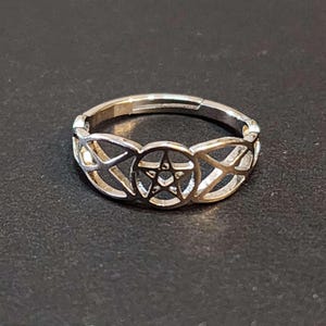 May include: A silver ring with a pentagram design. The ring is made of a thin metal and has a delicate, intricate design.