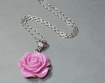 May include: A silver-toned chain necklace with a pendant featuring a pink rose. The rose pendant is detailed with petals and attached to the chain with a decorative bail. The necklace is displayed on a gray surface.