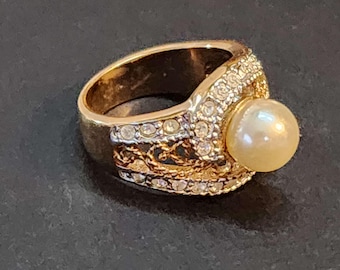 May include: A gold ring with a large pearl and a decorative design of small clear stones.