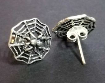 May include: A pair of silver spider web earrings with a spider in the center of the web. The earrings have a post and butterfly backing.