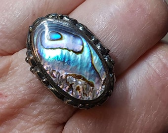 May include: A silver ring with an oval abalone shell inlay. The shell has iridescent blue, green, and purple colors.