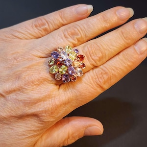May include: A gold ring with a flower design featuring a variety of colourful gemstones, including purple, red, green, and yellow.