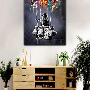 May include: A black and white painting of a child in a basket, holding onto colourful balloon-like shapes. The child is wearing a hooded jacket and is pointing to the right. The background is a dark grey with drips of paint.