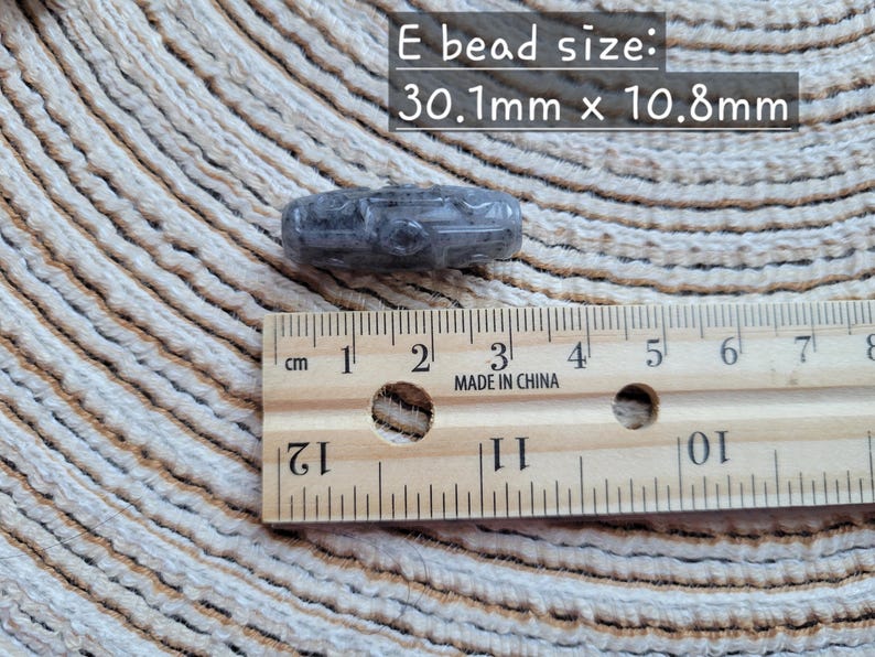 Puede incluir: Una cuenta gris tallada, de 3,01 cm x 1,08 cm, junto a una regla de madera marcada en cent&iacute;metros. El texto "E bead size: 30.1mm x 10.8mm" se muestra encima de la cuenta. La regla est&aacute; marcada "MADE IN CHINA".