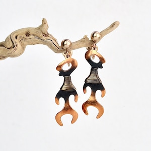 以下が含まれることがあります： 黒と茶色の抽象的なデザインが施されたゴールドトーンのイヤリングのペア。イヤリングはスタイリッシュな人間の姿の形をしています。