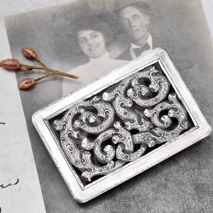 May include: A white ceramic mug with a black handle and the text "But First, Coffee" in a black, handwritten-style font. The mug is on a white surface.