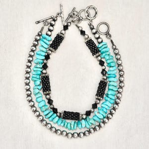 May include: A layered necklace with turquoise and black beads, silver beads, and silver clasps.