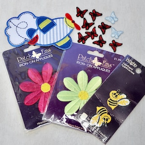May include: Assortment of iron-on appliques, including a blue and white airplane, red and black butterflies, pink and green flowers, and yellow and black bees. The appliques are packaged and ready to be applied.