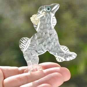 May include: A clear glass figurine of a stylised horse with a blue eye. The horse is standing on its hind legs with its front legs raised. The figurine is detailed with etched lines and has a smooth, polished finish.
