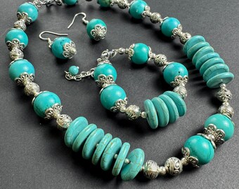 May include: A turquoise and silver jewelry set with a necklace, bracelet, and earrings. The necklace features large turquoise beads and a cluster of smaller turquoise beads. The bracelet has smaller turquoise beads and the earrings are simple turquoise studs.