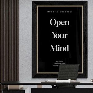 May include: A black framed motivational poster with the text "Road to Success: Open Your Mind" and the subtext "Be open. Be empathetic. Be ready." The poster is hanging on a wall in a modern office setting.