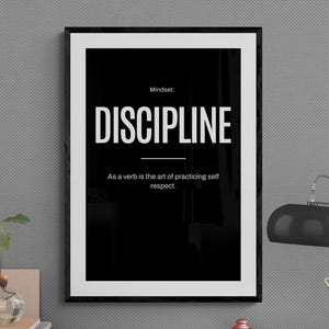 May include: A framed black and white print with the word "DISCIPLINE" in large, bold letters. The text below reads "As a verb is the art of practicing self respect." The print is on a desk with a lamp and other decorative items.