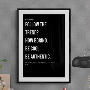 Könnte beinhalten: Ein gerahmter Schwarz-Weiß-Druck mit dem Text "FOLLOW THE TREND? HOW BORING. BE COOL, BE AUTHENTIC." Eine schwarze Schreibtischlampe mit sternförmigem Akzent steht auf einem Schreibtisch.