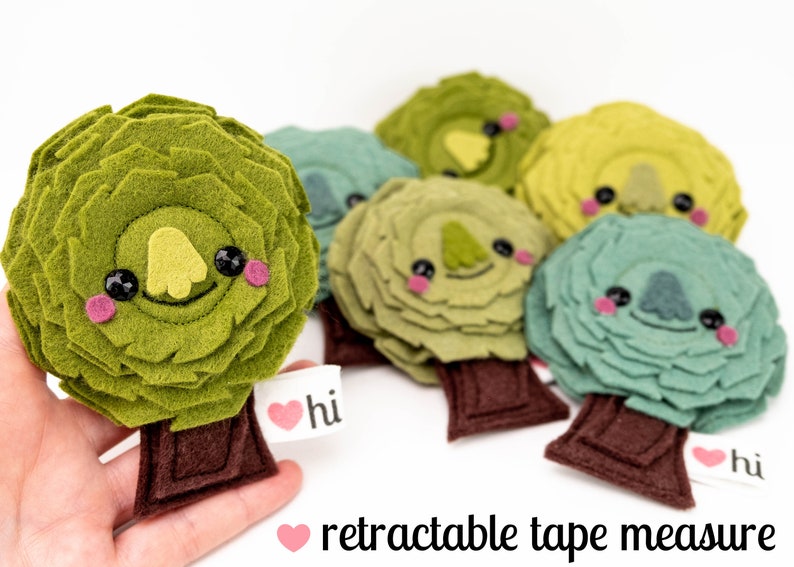 May include: A set of six felt tree ornaments with cute faces. Each tree is a different color, including green, blue, and yellow. The trees have brown felt trunks and are decorated with a heart and the word "hi".