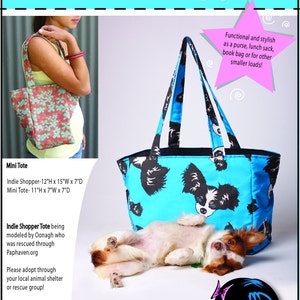 Puede incluir: Una bolsa de mano azul y negra con un estampado de perro. La bolsa mide 30,5 cm de alto, 38,1 cm de ancho y 17,8 cm de profundidad. La bolsa de mano está siendo modelada por una perra llamada Oonagh, que fue rescatada a través de Paphaven.org. El texto "Mini Tote & Indie Shopper" está en la parte superior de la imagen. El texto "Mackerilla Design" está en la parte inferior de la imagen. El texto "Where a good bag is never hard to find!" está debajo del nombre de la empresa.