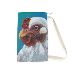 May include: A drawstring bag featuring a detailed illustration of a rooster's head. The rooster has white feathers, a red comb and wattle, and a yellow beak. The background is a gradient of blue and green.
