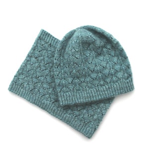 May include: A teal blue knitted hat and scarf set with a lacy pattern.