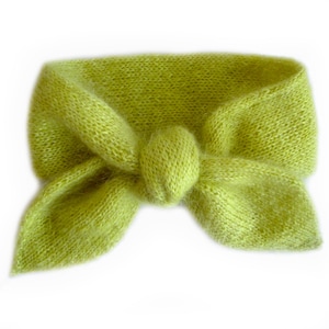 Può includere: Una fascia per capelli lavorata a maglia verde lime con un dettaglio a fiocco. La fascia è realizzata con un filato morbido e strutturato e presenta un nodo al centro. Il fiocco è formato da due anelli su entrambi i lati del nodo.