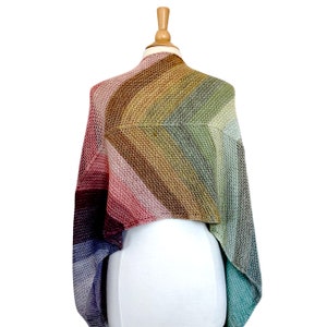 May include: A colourful crocheted shawl with a gradient of blue, purple, pink, brown, green and teal.