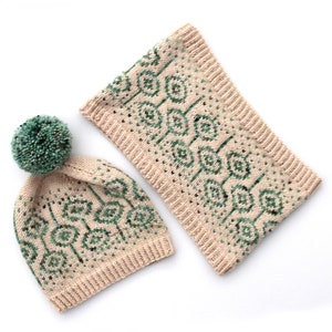 May include: A matching knit hat and neck warmer set. The hat has a teal pom-pom and a geometric pattern in teal and black on a beige background. The neck warmer has the same pattern. The set is made of a soft, knitted material.