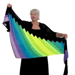May include: A colorful knitted shawl with a rainbow gradient pattern. The shawl is made with a black yarn and has a jagged edge.