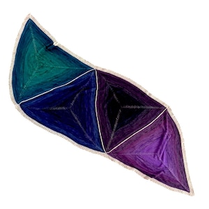 Op de afbeelding: Een driehoekige sjaal met een witte gehaakte rand. De sjaal is gemaakt van een gradient garen dat van teal naar donkerblauw naar paars overgaat.