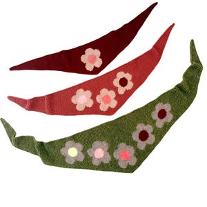May include: Three knitted neck scarves with floral designs. The scarves are in shades of red, pink, and green with pink and white flowers.