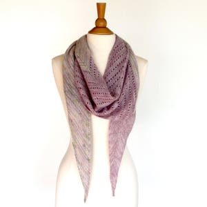 May include: A delicate, triangular shawl in a soft purple color with a subtle, multi-colored pattern. The shawl is draped over a wooden mannequin.