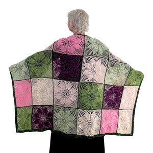 May include: A crocheted throw blanket with a patchwork design featuring squares in shades of pink, green, and purple. The blanket is made with a delicate, lacy stitch.