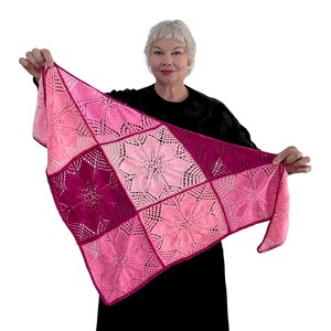 May include: A pink and burgundy crocheted shawl with a floral pattern. The shawl is made of squares with a delicate lace design.