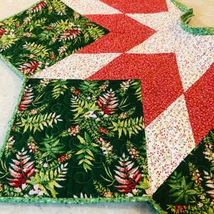 May include: A green, red, and white quilted Christmas tree skirt with a fern pattern. The skirt has a scalloped edge and is decorated with a starburst design.