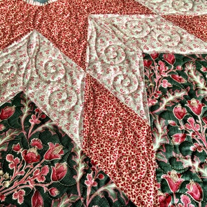 May include: Close-up of a quilted fabric with a star pattern. The fabric is made of different colours and patterns, including red, green, and white. The quilting is done in a swirl pattern.