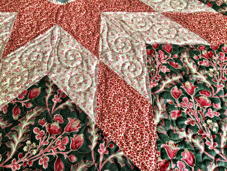 May include: Close-up of a quilted fabric with a star pattern. The fabric is made of different colours and patterns, including red, green, and white. The quilting is done in a swirl pattern.