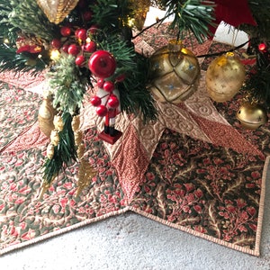 May include: A star-shaped quilted Christmas tree skirt in shades of green, red, and cream with a floral pattern. The skirt is decorated with gold ornaments and bells.