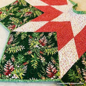 May include: A green, red and white quilted Christmas tree skirt with a fern pattern. The skirt has a scalloped edge and is decorated with a green ribbon.