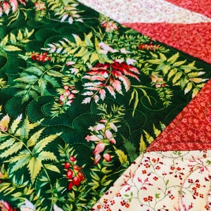 May include: A green fabric with a floral pattern featuring pink and red flowers and green leaves. The fabric is quilted with a decorative stitch. The fabric is sewn together with other fabrics in a patchwork pattern.