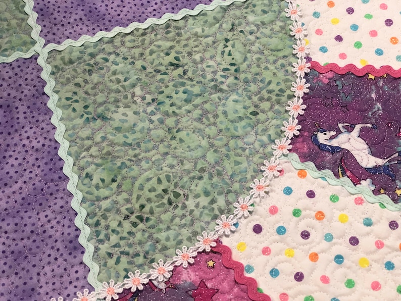 May include: A patchwork quilt with a variety of fabrics, including purple, green, white, and pink. The quilt is decorated with a white lace trim and features a unicorn design.