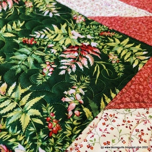 May include: A close-up of a quilt block featuring a green floral print fabric in the centre, surrounded by red and white floral print fabrics. The quilt block is quilted with a swirling pattern.