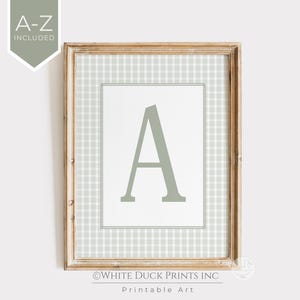 May include: A framed print featuring the letter "A" in a soft green hue. The letter is centered on a white background, framed by a light green and white checkered pattern. The wooden frame adds a rustic touch. The text "A-Z INCLUDED" is in the upper left corner.