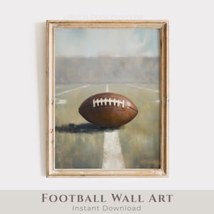 Puede incluir: Obra de arte enmarcada que presenta un balón de fútbol americano marrón sobre un campo verde con líneas blancas. La pintura tiene una estética vintage, con una paleta de colores neutros y un fondo suave y borroso. El texto "FOOTBALL WALL ART" está en la parte inferior.