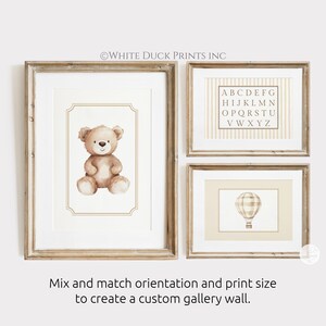 May include: Three framed prints with a nursery theme. One features a watercolor teddy bear, another an alphabet chart, and the third a hot air balloon. The frames are light brown. Text on the image reads: Mix and match orientation and print size to create a custom gallery wall.