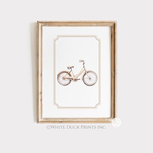 May include: A framed print showing a watercolour illustration of a cream-coloured bicycle. The bicycle has a classic design with curved handlebars and a step-through frame. The print is set against a white background with a decorative border, and the frame is a light wood colour. The text "WHITE DUCK PRINTS INC" is at the bottom.