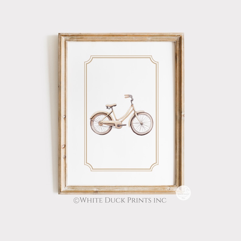 May include: A framed print showing a watercolour illustration of a cream-coloured bicycle. The bicycle has a classic design with curved handlebars and a step-through frame. The print is set against a white background with a decorative border, and the frame is a light wood colour. The text "WHITE DUCK PRINTS INC" is at the bottom.