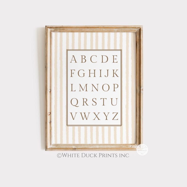 May include: A framed alphabet print with a light wood-coloured frame. The background has vertical beige and white stripes. The letters are in a serif font. The text "WHITE DUCK PRINTS INC" is at the bottom.