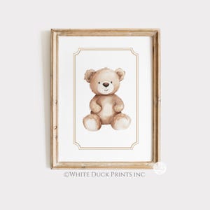 May include: A framed print with a watercolour illustration of a teddy bear. The bear is light brown with a white belly and paws, and a small black nose. The frame is a light wood colour, and the print has a white border.