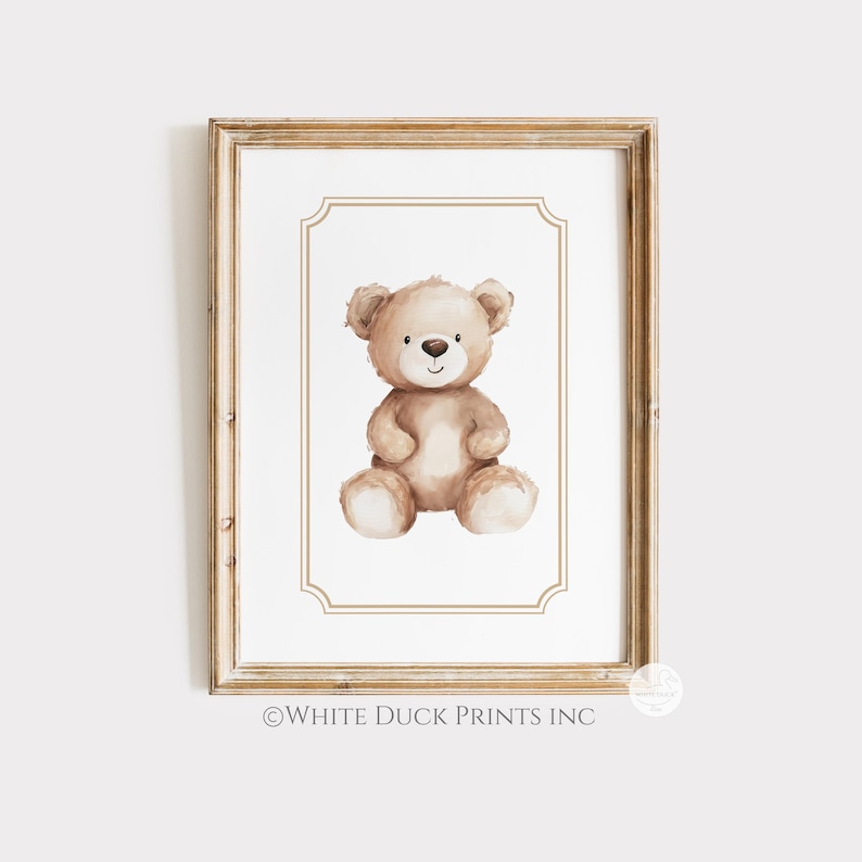 May include: A framed print with a watercolour illustration of a teddy bear. The bear is light brown with a white belly and paws, and a small black nose. The frame is a light wood colour, and the print has a white border.